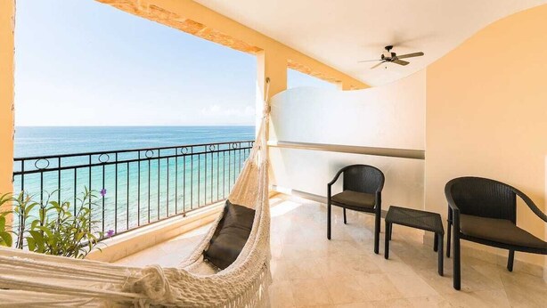 A balcony with a view of the ocean, a hammock, and two chairs.