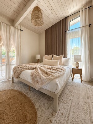Quarto com cama, mesas de cabeceira, luminária pendente e vista pela janela.