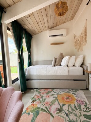 Un dormitorio con cama, ventana con cortinas, aire acondicionado instalado en la pared y un tapiz de macramé.