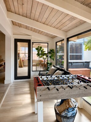 Una sala moderna con techo de madera, una mesa de fútbol de mesa, un sofá cómodo y un ventanal con vistas al exterior.