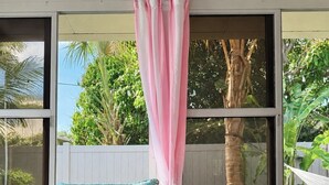 Un banco de madera con dos cojines florales, una mesa de madera con una planta y vistas al verdor a través de una ventana.