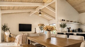 Amplia sala de estar con mesa de comedor de madera, asientos cómodos, televisor y cocina al fondo.