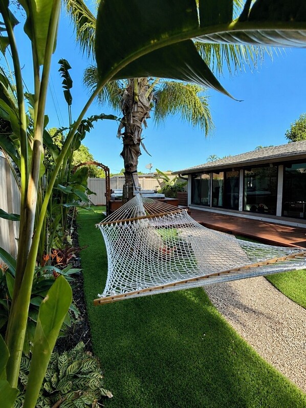 Una hamaca en un jardín con una palmera y una casa al fondo.