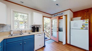 A compact kitchen with a sink, stove, and refrigerator, wooden flooring, and a sign reading "OUR HAPPY PLACE".