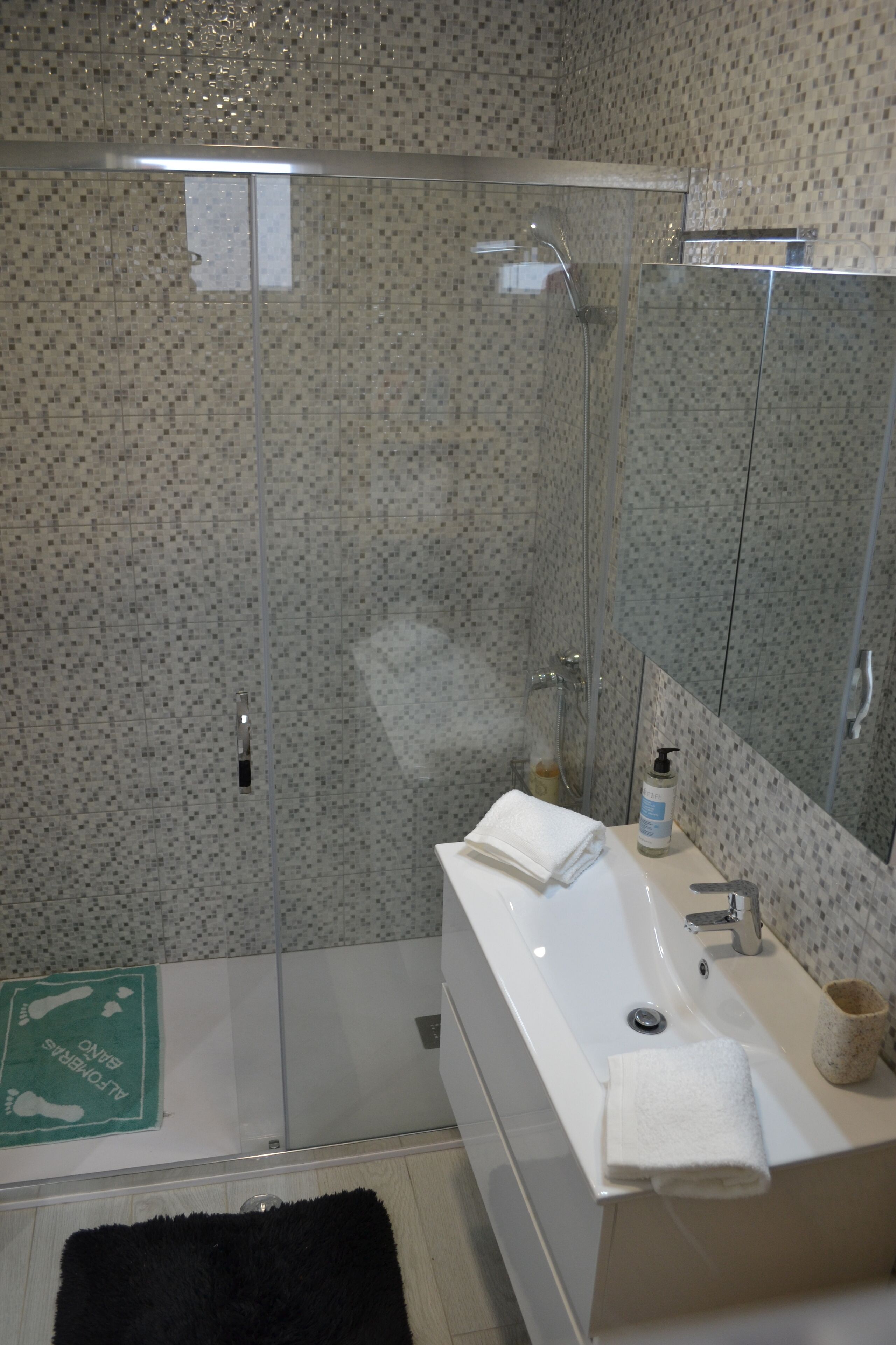 A modern bathroom with a glass shower enclosure, a white sink, and a mirror.