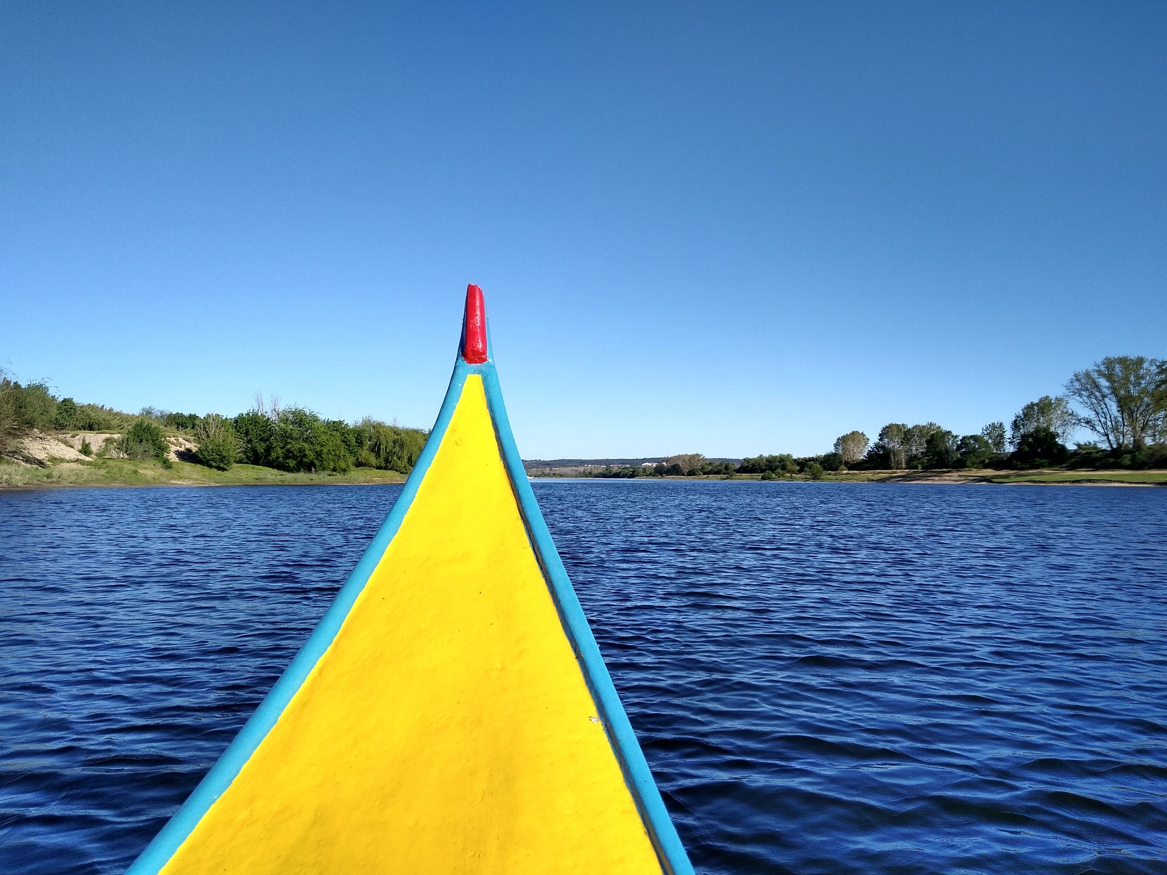 A canoe with a red tip and yellow and blue body, floating on a calm body of water.