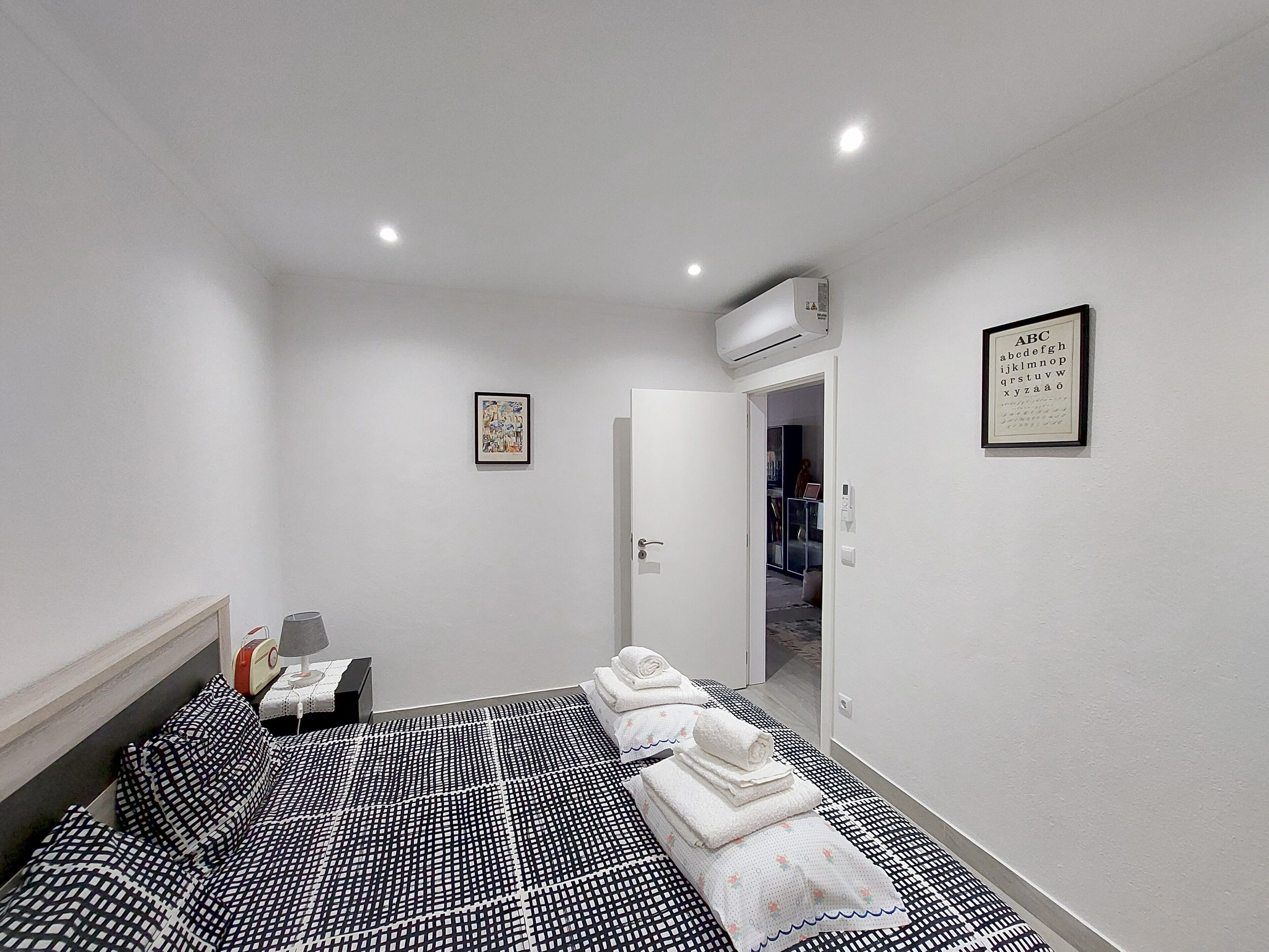 A bedroom with a bed, a desk, and a chair. There is a door leading to another room.