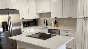 A modern kitchen with white cabinets, stainless steel appliances, a central island with stools, and a pet feeding station. - Charming 1BR Retreat in Denver (Denver)