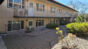 A two-story building with a balcony on the upper floor, a paved courtyard, and a small garden area. - Charming furnished 2-bedroom, 1 bath apartment with WiFi, AC in lovely Kalispell (Kalispell)