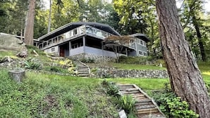 A two-story house with a sloped roof, surrounded by trees and a stone wall.