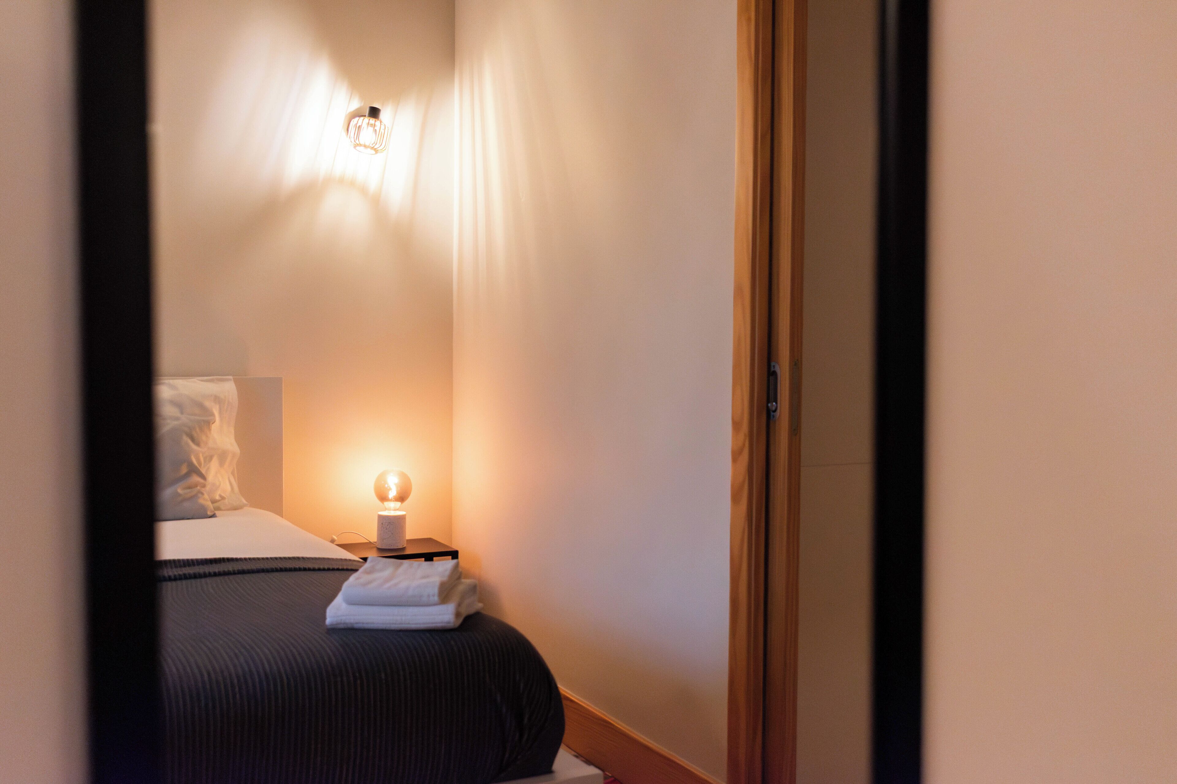 Une chambre d’hôtel avec un lit, une table de chevet avec une lampe et une porte.
