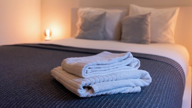 Una cama bien hecha con una toalla doblada y una lámpara de noche.