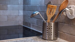 Un porta utensilios de acero inoxidable con herramientas de cocina de madera y metal frente a un salpicadero de azulejos.