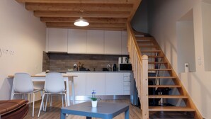 Una cocina moderna con armarios blancos, una escalera de madera y un comedor con mesa y sillas.