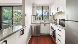 A modern kitchen with white cabinets, stainless steel appliances, and a large window overlooking greenery.