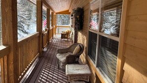 Una terraza de madera con mobiliario de mimbre y vistas a árboles cubiertos de nieve.