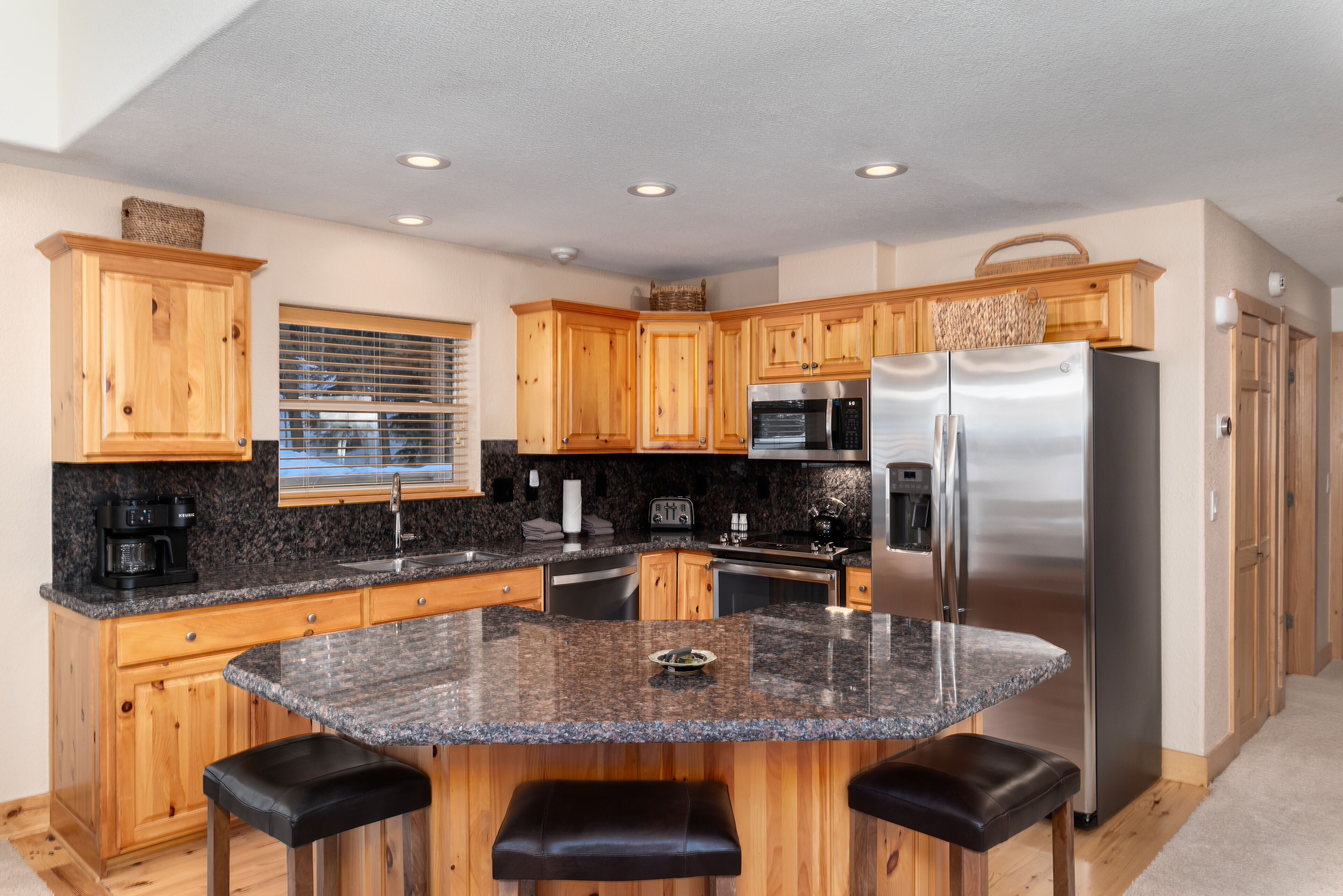 A modern kitchen with wooden cabinets, granite countertops, stainless steel appliances, and a central island with bar stools.