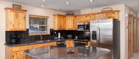 A modern kitchen with wooden cabinets, granite countertops, stainless steel appliances, and a central island with bar stools.