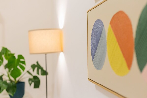 Ein gerahmtes Kunstwerk mit abstrakten Formen, eine Stehlampe und ein Blumentopf.