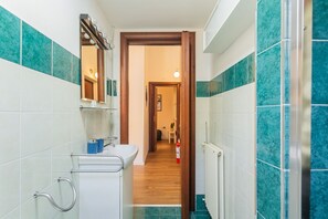 Ein schmales Badezimmer mit einem weißen Waschbecken, einem Spiegel und einer Holztür, die zu einem Flur führt.