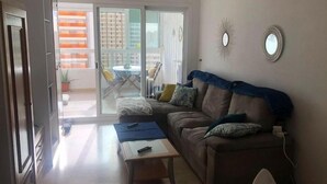 A living room with a sofa, a coffee table, and a TV. There is a sliding glass door leading to a balcony with a table and chairs. - Gemelos 22, Benidorm-Alicante (Benidorm)
