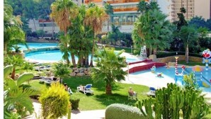 A resort with a pool area, palm trees, and a view of high-rise buildings in the background. - Gemelos 22, Benidorm-Alicante (Benidorm)