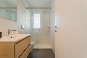 Ein modernes Badezimmer mit Duschkabine aus Glas, einem weißen Waschbecken und einem Holzboden.