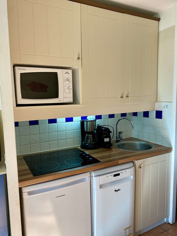 A compact kitchen with white cabinets, a microwave, a coffee maker, a sink, and a dishwasher.