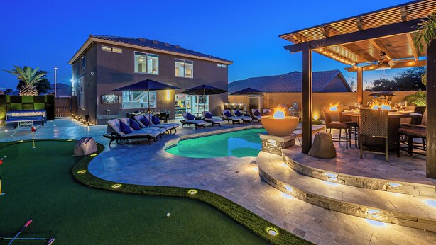 Ein Poolbereich mit Liegestühlen, einem kleinen Putting Green und einer überdachten Lounge mit Feuerstelle.