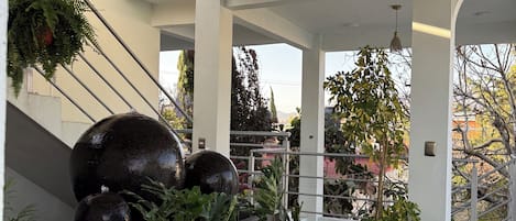 Área externa coberta com escadaria, plantas em vasos e um espelho d'água.