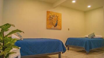 Two single beds with blue bedding in a room with a peacock painting on the wall.