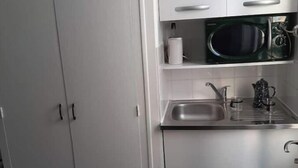 A kitchen with white cabinets, a stainless steel sink, a microwave, and a kettle. - Studio - M° Garibaldi - 20 mn Champs-Élysées (Saint-Ouen-sur-Seine)