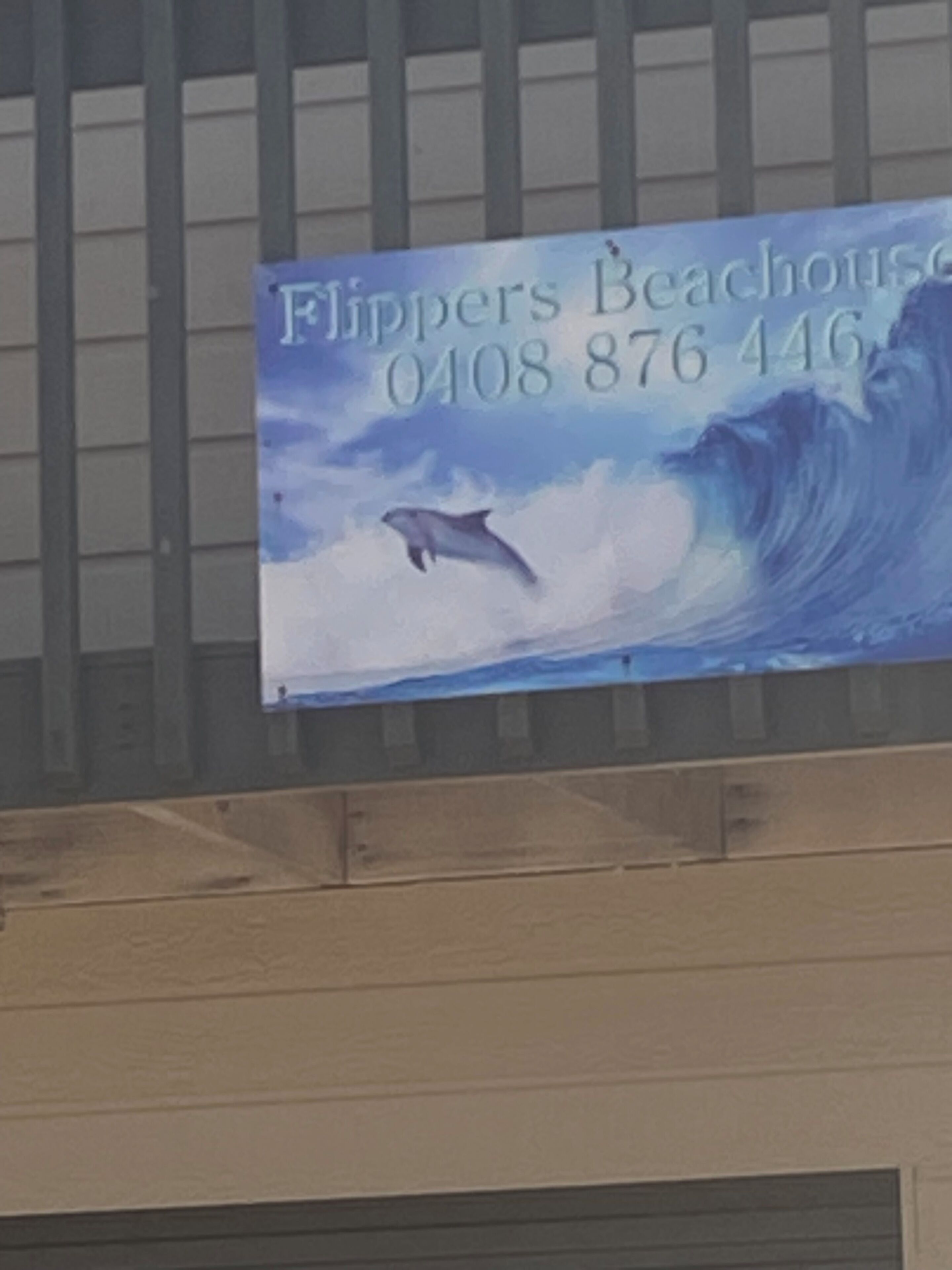 A sign for 'Flippers Beachhouse' with a phone number.
