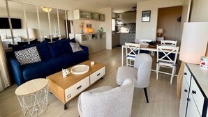A modern living room with a blue sofa, a coffee table, and a dining area with white chairs and a table. - QUIBERON - T2 - 50m2 - Port-Haliguen (QUIBERON)