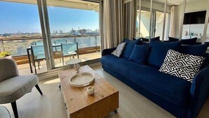 A modern living room with a blue sofa, a wooden coffee table, and a view of the city through large windows. - QUIBERON - T2 - 50m2 - Port-Haliguen (QUIBERON)
