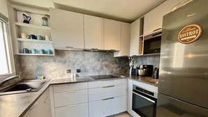 A modern kitchen with white cabinets, a stainless steel refrigerator, and a built-in oven. - QUIBERON - T2 - 50m2 - Port-Haliguen (QUIBERON)