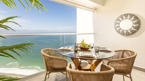 Un balcón con una mesa de vidrio, sillas de mimbre y vista al mar.