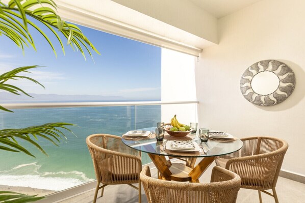 A balcony with a glass table, wicker chairs, and a view of the sea.