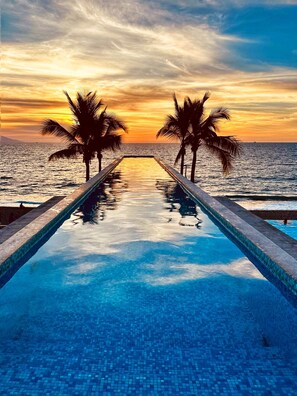 A infinity pool with a view of the ocean and palm trees at sunset. - Dreamy Oceanview Getaway  1BR + Breakfast Included (Puerto Vallarta)