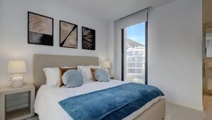 A modern bedroom with a large bed, white bedding, and a view of buildings through a large window. - Bossa Nova | pool - terrace - fuengirola (Fuengirola)