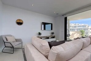 A modern living room with a sofa, a chair, a flat-screen TV mounted on the wall, and a view of the outside. - ViVi Homes pool, Bossa nova apartment (Fuengirola)