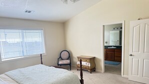 Une chambre à coucher comprenant un lit, une chaise, une commode et une porte donnant sur une salle de bain.