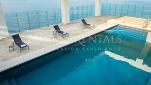 A pool with clear blue water, surrounded by glass railings and lounge chairs.