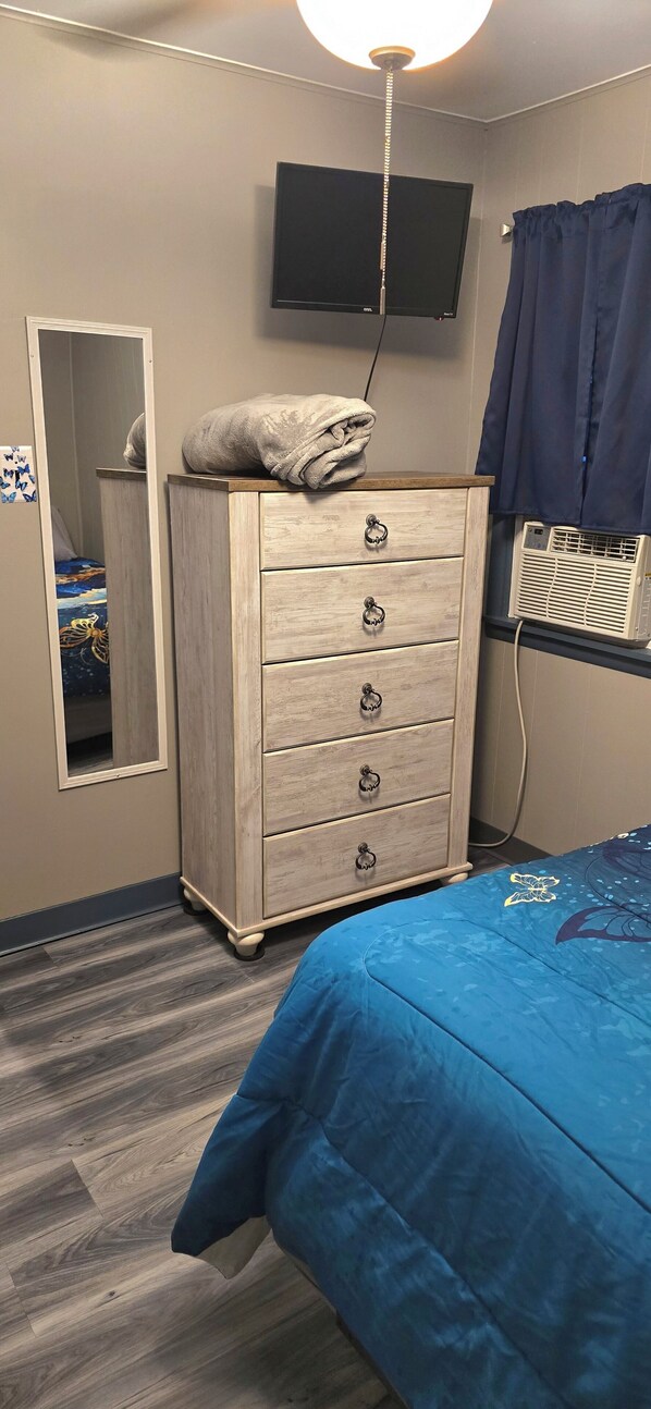 A bedroom with a bed, a dresser, a mirror, a television, and a window with curtains.