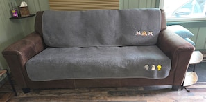 A brown leather sofa with a grey blanket, a wooden floor, and a window with blinds.