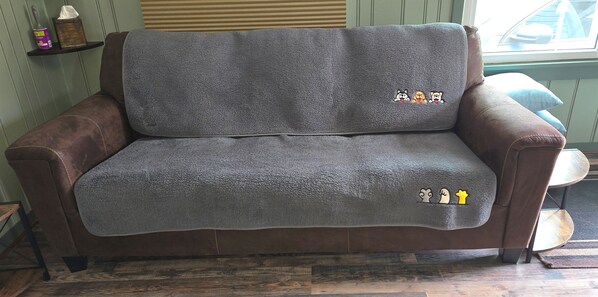 A brown leather sofa with a grey blanket, a wooden floor, and a window with blinds.