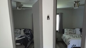 A room with a wooden floor, a bed with a white and black patterned bedspread, a ceiling fan, and a visible light switch on the wall. - "Oreo’s Dream – A Cozy, Dog-Lover’s Retreat!" (Geneva)