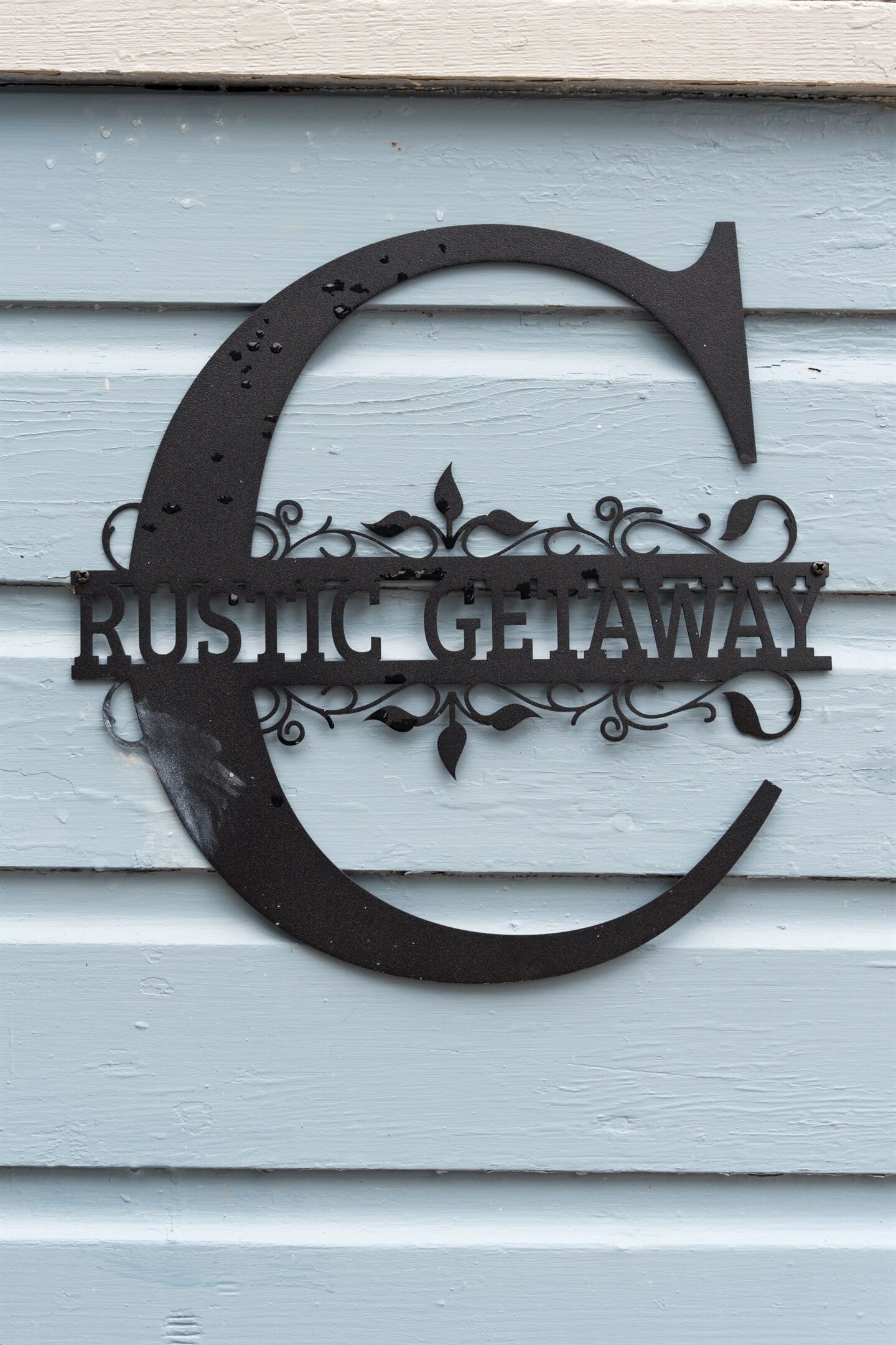 A metal sign with the words "Rustic Getaway" on a light blue wooden background.