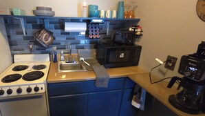 Una cocina compacta equipada con estufa, lavamanos, microondas y cafetera.