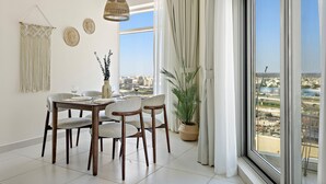 Ein Essbereich mit Tisch für vier Personen, einer hängenden Wanddekoration aus Makramee und Blick auf eine Stadtkulisse durch große Fenster.